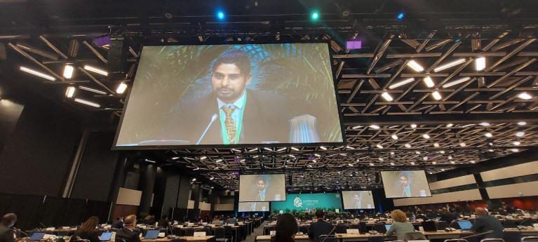 The speaker is displayed on a big screen in a conference room.